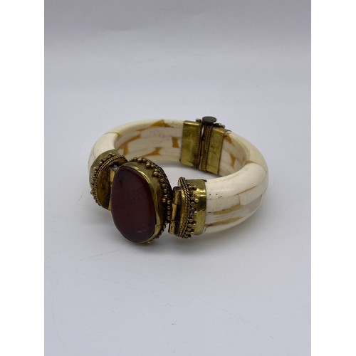 690 - THREE PLATED AND GOLD TONE COLOURED BANGLES (INC. BADEN EXAMPLE) AND AN ORNATE BONE BANGLE WITH RED ... 