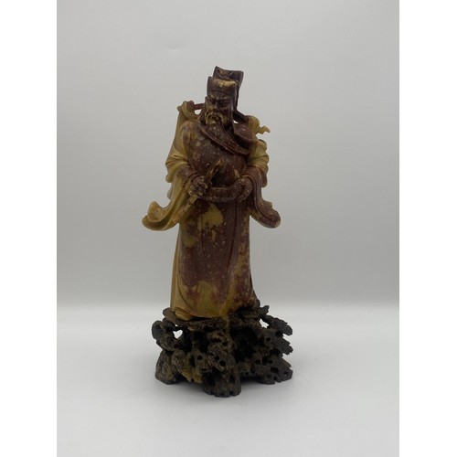 557 - ORIENTAL CARVED RUSSET SOAPSTONE FIGURE OF AN EMPEROR ON A ROCK WORK BASE