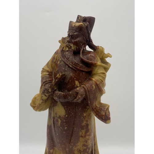 557 - ORIENTAL CARVED RUSSET SOAPSTONE FIGURE OF AN EMPEROR ON A ROCK WORK BASE