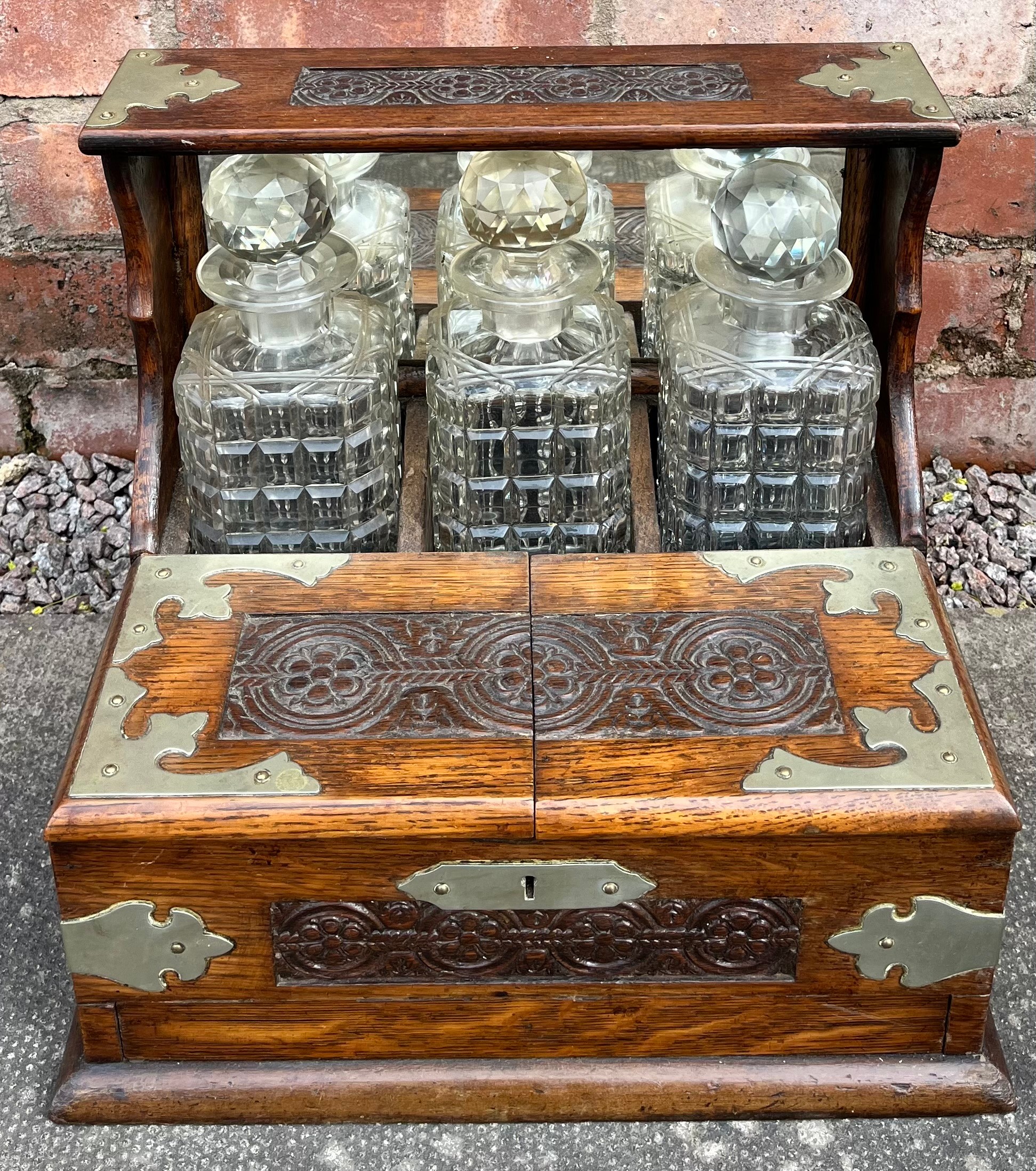 OAK FRAMED CARVED PANEL TANTALUS FITTED WITH GLASS DECANTERS (NO KEY)