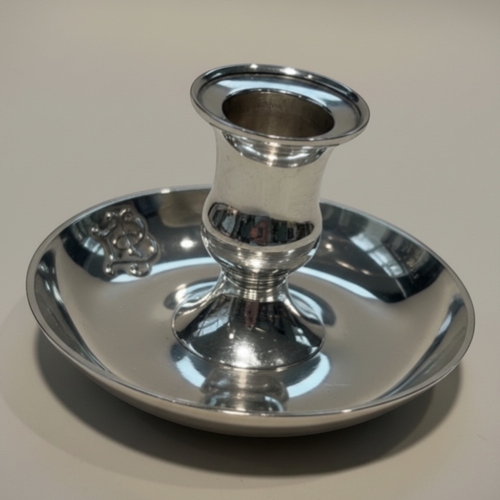 A George VI sterling silver chamberstick, hallmarked Birmingham, 1940, by Sanders & Mackenzie. Of circular form, the piece features a central nozzle set within a wide drip pan with a simple rounded rim. A robust and elegant example of early wartime British silver, combining practical utility with the renowned craftsmanship of the Birmingham jewellery quarter. Maker: Sanders & Mackenzie Origin: Birmingham, UK Material: .925 Sterling Silver Year: 1940 Weight: 93g Condition: Very Good; hallmarks are clear, no major dentsor repairs. Auctioneer's Note: Rare to find domestic silver produced during the height of the 1940 wartime era in such clean condition.