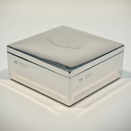 A substantial George V sterling silver presentation box of heavy-gauge construction, hallmarked Birmingham, c. 1910– 1920. Of elegant square form with a hinged lid, the cover is centred with an engraved heraldic crest featuring a crown over a landscape. The box possesses a satisfying weight and a deep, historic patina. Origin: Birmingham, UK. Date: Early 20th Century. Weight: 306g. Dimensions: 8.5cm x 8.5cm x 5cm. Condition: Good antique condition; the heraldic engraving and hallmarks show softening and wear consistent with age and frequent polishing; hinge remains strong and the lid closes flush. Auctioneer's Note: The "heavy-gauge" nature of this box setsit apart from more common, thinner-walled cigarette boxes. The faded crest provides an intriguing glimpse into its provenance, making it a wonderful piece for a collector of historical British silver.