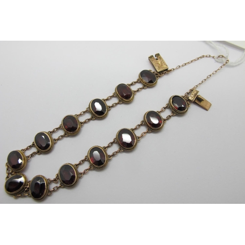 103 - A Garnet Set Bracelet, composed of thirteen oval collet set garnets, on two row fine chain connectio... 