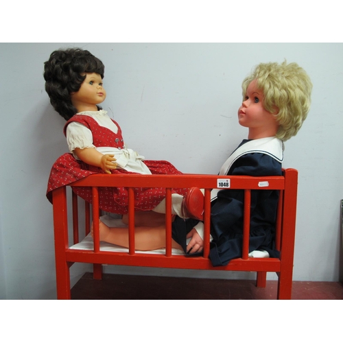 1048 - A Pedigree Walking Doll, together with one other doll, in a red cot.