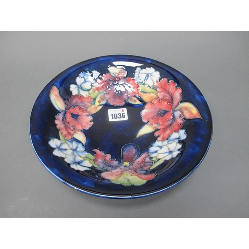 1036 - A Moorcroft Pottery Shallow Circular Bowl, painted with the 'Orchid' pattern against a dark blue gro... 