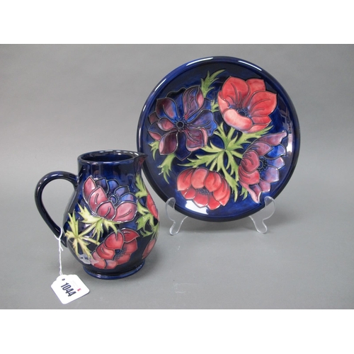 1044 - A Moorcroft Pottery Plate, painted in the 'Anemone' pattern with pink and purple flowers against a d... 