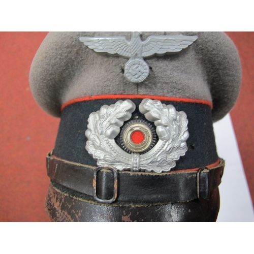 566 - A WWII German N.C.O Peaked Cap, with red artillery piping, metal wreath, cockade and Nazi Eagle incl... 