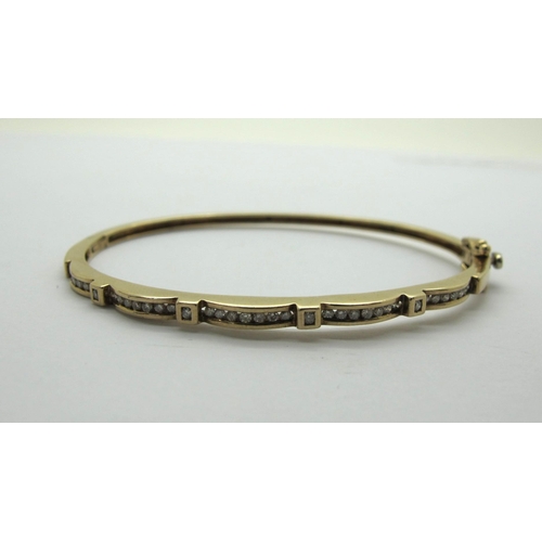 192 - A Modern 9ct Gold Diamond Set Hinged Bangle, channel set with uniform stones, hinged to snap clasp (... 