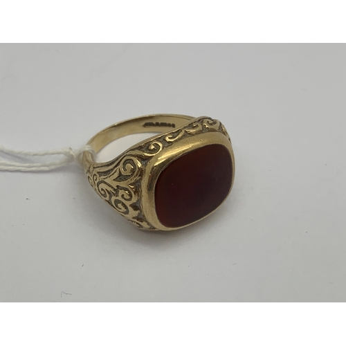 119 - A 9ct Gold Polished Hardstone Inset Gent's Ring, cushion shape panel rubover set, between scroll det... 