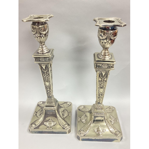 6 - A Pair of Highly Decorative Plated Candlesticks, each of Classical style detailed in relief with ram... 