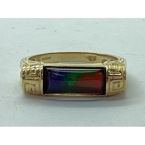 54 - Korite; An Ornate Ammolite Set Ring, the elongated panel semi set between greek key style bifurcated... 