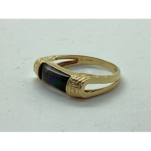 54 - Korite; An Ornate Ammolite Set Ring, the elongated panel semi set between greek key style bifurcated... 