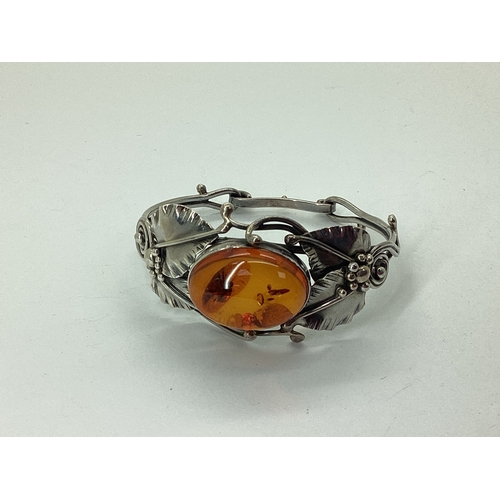 93 - An Amber Inset Openwork Bangle, oval collet set to the centre, within textured leaf design setting, ... 