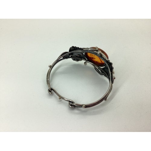 93 - An Amber Inset Openwork Bangle, oval collet set to the centre, within textured leaf design setting, ... 