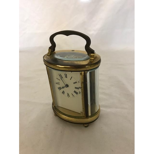 240 - A carriage clock, white enamel dial, in an oval brass and bevelled glass case