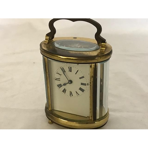 240 - A carriage clock, white enamel dial, in an oval brass and bevelled glass case