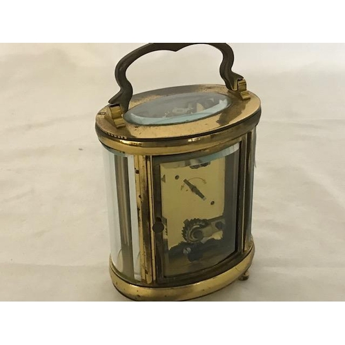 240 - A carriage clock, white enamel dial, in an oval brass and bevelled glass case