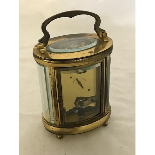 240 - A carriage clock, white enamel dial, in an oval brass and bevelled glass case