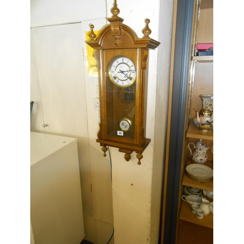 44 - A modern wall clock with white enamel dial, in a walnut finished case with turned finials, glass pan... 