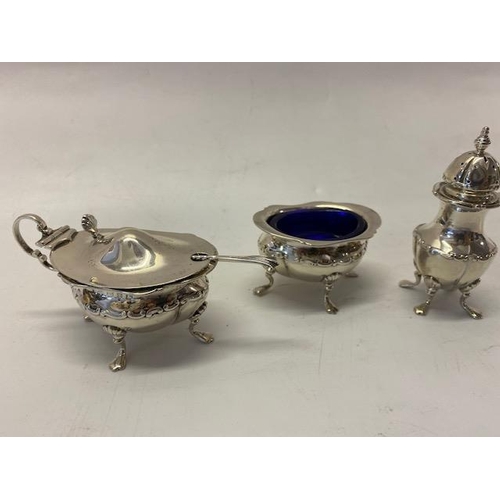 206 - A silver three piece cruet with repousse decoration of leaf scrolls, on pad feet, complete with spoo... 