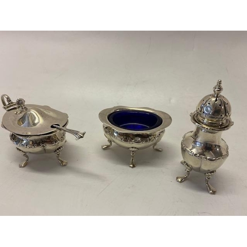 206 - A silver three piece cruet with repousse decoration of leaf scrolls, on pad feet, complete with spoo... 