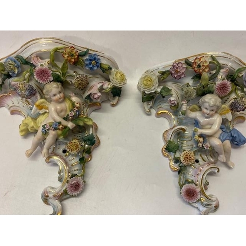 167 - A pair of Continental porcelain wall brackets of cornucopia form with flower encrusted and cupid dec... 