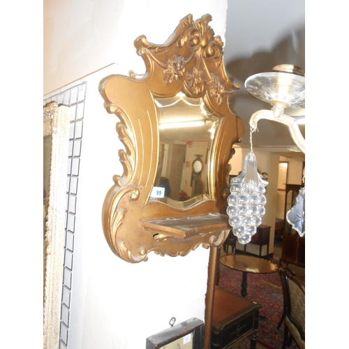 99 - A pair of wall mirrors in gilt frames with flower decoration, each fitted shelf