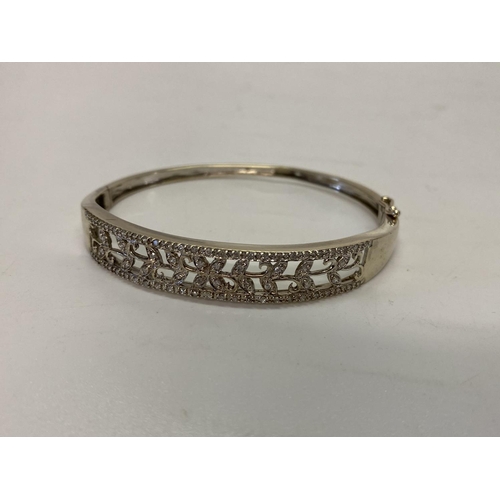 218 - A lady's 10kt. white gold hinged bangle, the pierced top set diamonds to flower and leaf design