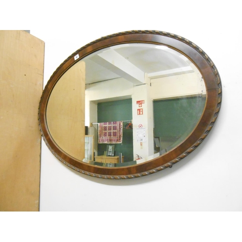 41 - An oval bevelled wall mirror in a mahogany frame with ribbon tie decoration - 27in. x 38in.