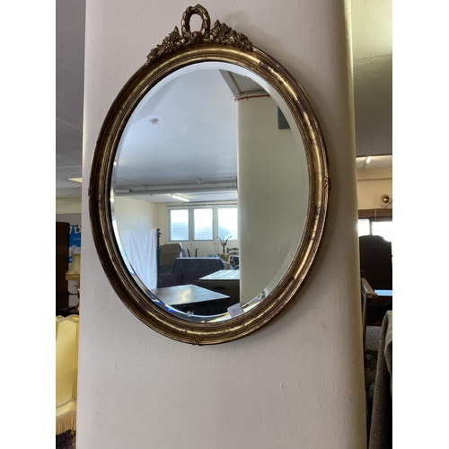 83 - An arched bevelled wall mirror in a gilt frame and an oval wall mirror in a gilt frame with ribbon t... 