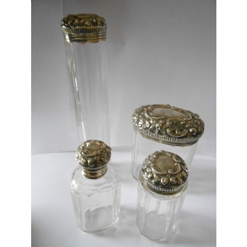 194 - Four glass toilet bottles with repousse decorated silver lids and a matching rectangular silver cove... 
