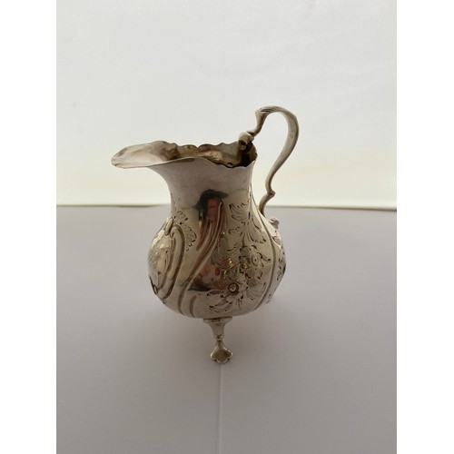 244 - A Victorian silver cream jug with serrated edge, leaf clad handle, repousse decorated flowers, on th... 