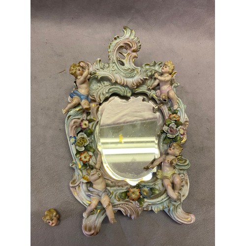 122 - A small Continental porcelain dressing table mirror with applied cupids, flowers and leaf decoration... 