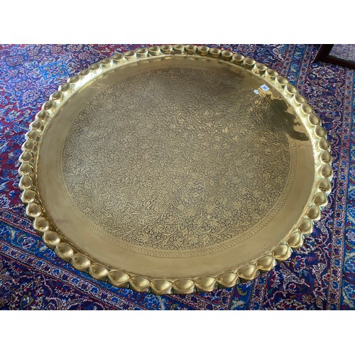 51 - A large brass tray with shaped edge, on folding wooden base - 38in. dia.