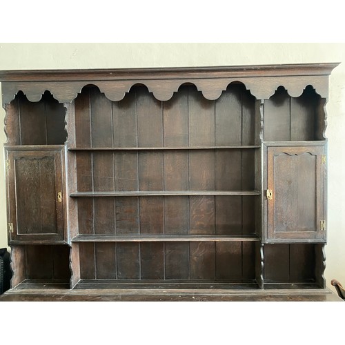 57 - An antique oak dresser, the upper part fitted shelves and cupboards, the base with shaped apron, fit... 