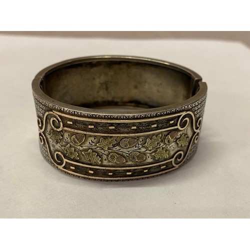 282 - A silver coloured metal stiff hinged bangle, the front decorated with acorns and oak leaves