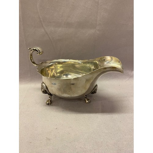 230 - A large Mappin and Webb silver sauce boat with serrated edge, leaf clad scroll handles, raised on th... 