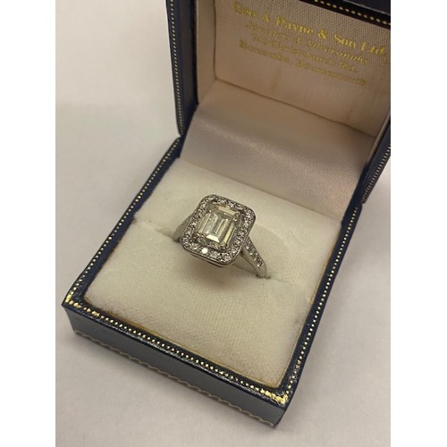 193 - A lady's ring set centre emerald cut diamond surrounded by diamonds, diamond set shoulders, on an 18... 