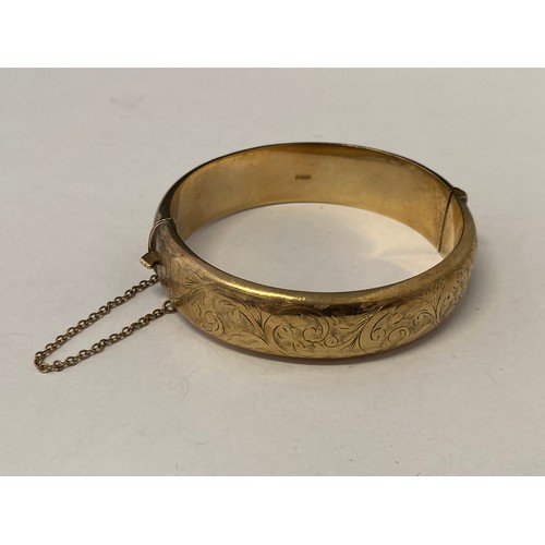 233 - A 9ct. gold hinged bangle with engraved decoration
