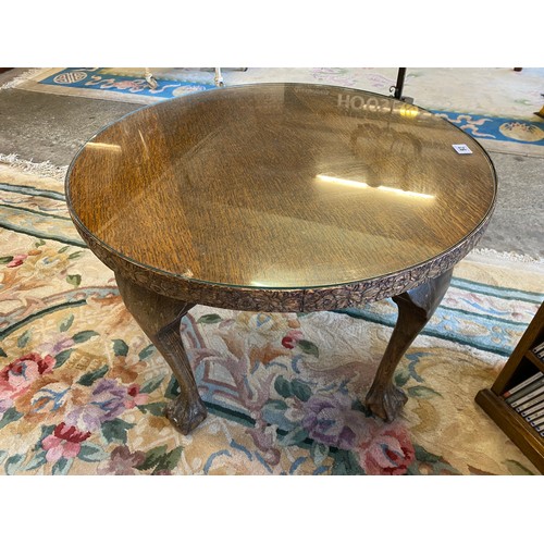 92 - An oak occasional table with circular top and glass top, carved frieze, on cabriole legs terminating... 