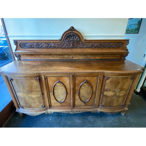 16 - A large 1930's walnut sideboard, the raised shaped back with carved decoration of basket and bowls o... 