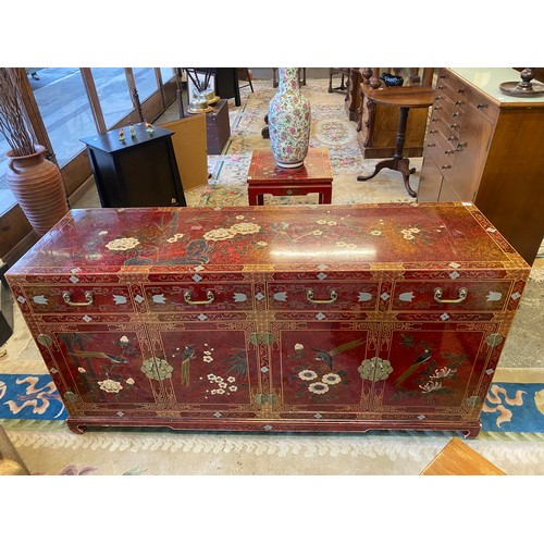 23 - A modern Chinese red lacquered sideboard with gilt and floral decoration fitted three frieze drawers... 