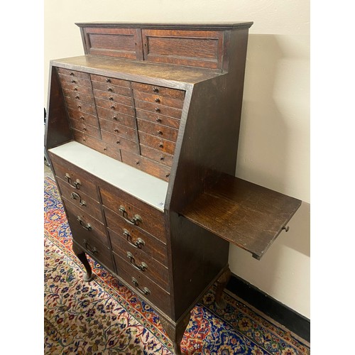 72 - An early 20th Century oak dentists cabinet, the top fitted two small doors above twenty three narrow... 