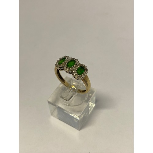 255 - A lady's ring set three oval emerald coloured stones surrounded by diamonds, on a 9ct. gold shank