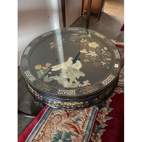 21 - A circular black lacquered coffee table, the top with soapstone style decoration of flowers and two ... 