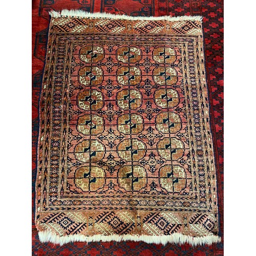 6 - A small Bokhara style rug, red field with eighteen medallions to the centre within black and white g... 