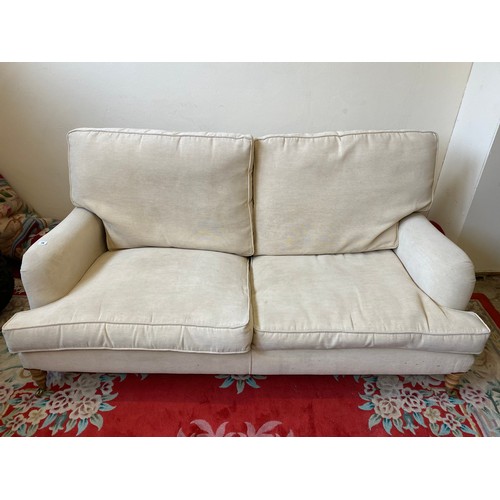 79 - A modern two seater settee upholstered in beige material with loose seat and back cushions, on turne... 