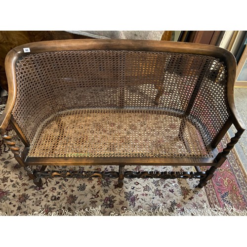 83 - An oak finished two seater settee with cane seat and back, barley twist supports and legs united by ... 