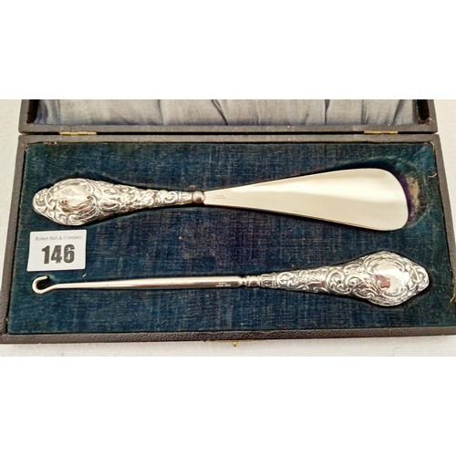 146 - A cased set of shoe horn and button hooks, with profusely embossed silver handles