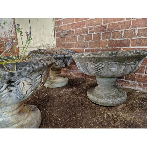 505 - Three simulated stone pedestal urns with vine leaf detail